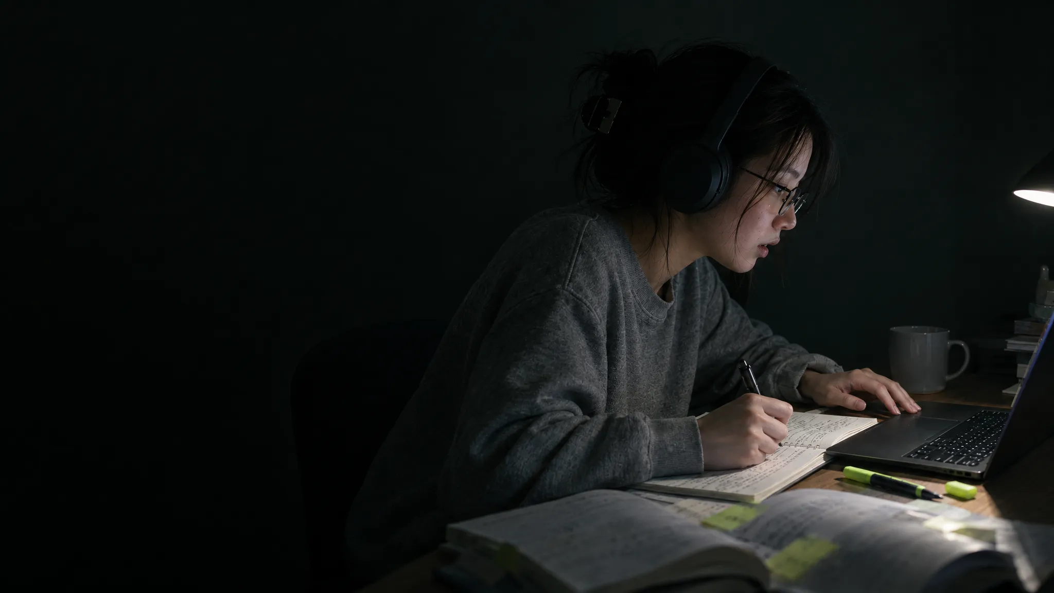 夜、自分の部屋でヘッドホンを付け、ノートPCでレッスンを聞き返しながらノートに書き込む女性